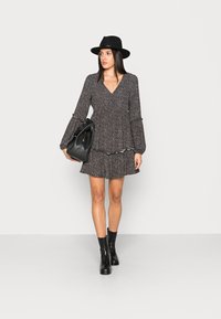 Vestido com padrão preto e branco, com mangas largas, decote em V e saia com camadas de babados; acompanhado de um chapéu preto e bolsa de couro.