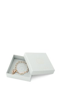 Gouden metalen kettingarmband met een bedel, gepresenteerd in een lichtgrijze, gestructureerde cadeauverpakking met een geperst logo.