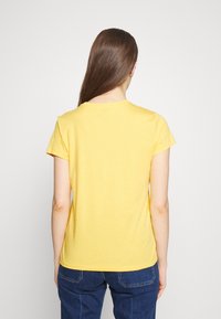 Gul bomullströja med korta ärmar och rundad halsringning, med en slät yta. Bakifrån syns en enkel, odekorerad design.