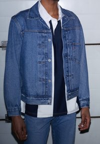 Jeansjacka i mellanblått, med knäppning fram, två bröstfickor och en avslappnad passform. Kombinerad med en randig skjorta i marinblått och vitt under.