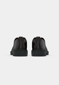 Pair of dark brown leather shoes with thick black soles shown from the back on a plain light gray background.
