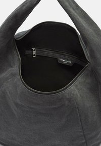 Czarna torba z tkaniny o zaokrąglonym kształcie i miękkiej teksturze. Wnętrze zawiera kieszeń na zamek błyskawiczny oraz metkę marki, z prostym metalowym zamkiem.