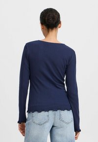 Marineblaues, geripptes Langarmoberteil mit einem gewellten Saum und besonderen Manschettendetails, aus elastischem Stoff gefertigt. Besitzt einen weiten Rundhalsausschnitt und eine figurbetonte Silhouette.