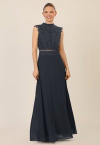 Abito blu navy con corpino in pizzo, bordi ondulati, scollatura alta e gonna fluida. Presenta maniche a cappuccio e dettagli in pizzo intricati.