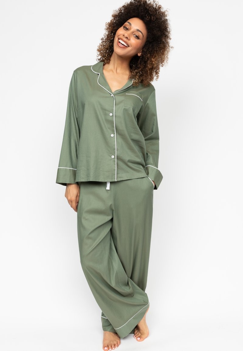 Olivegrünes Schlafanzug-Set aus weichem Stoff. Es besteht aus einem knöpfen Shirt mit Tasche und weit geschnittenen Hosen mit weißen Paspelierungen.