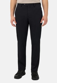 Juoda kelnė su medvilnės mišinio audiniu, plokščiu priekiu, standartinėmis kišenėmis ir klasikinio kirpimo, derinama su juodais sportbačiais.