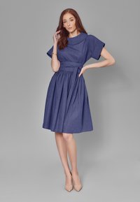 Jeansowa sukienka w głębokim granacie z plisowaną spódnicą, krótkimi rękawami, szerokim kołnierzem i związanym paskiem w talii; gładka tekstura, do kolan.