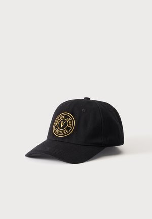 Casquette de baseball noire avec une visière incurvée ornée d'un emblème rond doré portant l'inscription « Versace Jeans Couture » à l'avant.