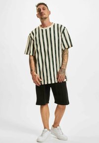 Striped short-sleeve shirt in off-white and green, paired with black shorts and white sneakers. Features bold vertical lines and relaxed fit.
