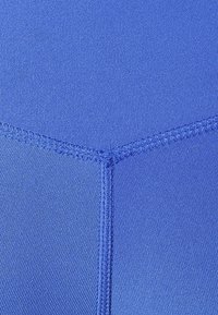 Modrý textil s hladkou strukturou; má ploché švy a detail ve tvaru vlaštovky uprostřed. Jednotná barva po celém povrchu.