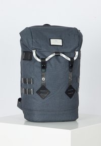 Sac à dos en tissu gris avec un design à rabat, accents noirs externes et fermeture à cordon à motif. Comprend des sangles latérales et un patch logo.