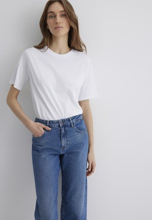 White short-sleeve t-shirt paired with high-waisted blue jeans. The jeans feature a button closure and front pockets with a classic denim texture.
