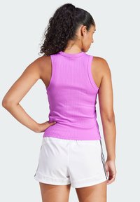 Geribbelde, mouwloze tanktop in felroze met een hoge halslijn, strakke pasvorm en een gladde textuur, gecombineerd met witte sportshorts.