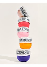 Fünf bunte gestapelte Sol de Janeiro Hautpflege-Cremedosen in den Farbtönen Lila, Orange, Pink, Rot und Roségold mit weißen Etiketten.