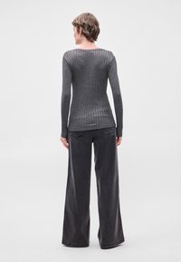 Γκρι ριπ ψηλόμεσο τοπ με μακριά μανίκια και εφαρμοστή σιλουέτα, σε συνδυασμό με ψηλόμεσο παντελόνι σε στυλ καμπάνα σε σκούρο γκρι, και τα δύο φτιαγμένα από μαλακό ύφασμα.