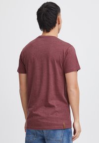 Camiseta corta de manga marón, diseño de cuello redondo, hecha de tela texturizada, con una pequeña etiqueta marrón de la marca en el lado inferior, combinada con pantalones cortos de mezclilla.