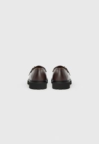 Chaussures en cuir marron avec une finition texturée, semelles en caoutchouc noir et forme arrondie. Présentent de petites découpes près du talon pour un détail de design.