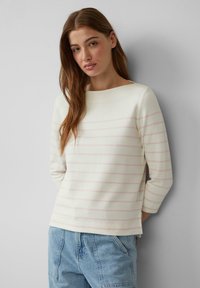 Witte lange mouwen top met lichtroze horizontale strepen, ronde halslijn, zachte textuur, gedragen met lichtblauwe denim onderkant.
