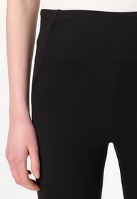 Zwarte leggings van rekbaar materiaal met een hoge taille, met een gladde textuur en gestikte details langs de naden.