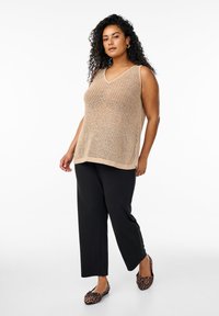 Beige pletený bezrukávový top s dekoltem ve tvaru V, kombinovaný s černými širokými kalhotami a plochými botami s leopardím potiskem. Hladká textura, volný střih.