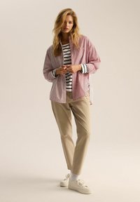 Czerwono-biała, w paski, oversize'owa koszula nałożona na czarno-biały, paskowany top, w komplecie z beżowymi spodniami i białymi sneakersami.