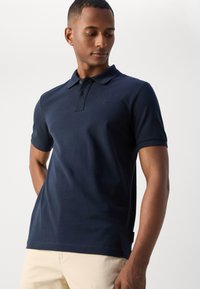 Marineblå polo skjorte laget av bomull, med krage, korte ermer, tre-knapps placket og en subtil logo på brystet.