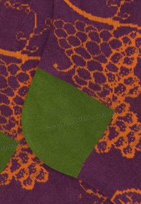 Calzini viola con un motivo di uva arancione, con tallone e punta verdi. La texture è morbida e sono visibili dettagli del motivo a maglia.