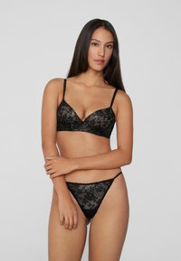 Černá krajková prádlo obsahující podprsenku s hlbokým výstřihem a nastavitelné ramínka spolu se sexy tangy. Elegantní květinový vzor s průhlednou texturou.
