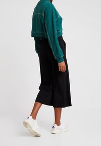 Teal kortärmad sweatshirt med vit sömnad, ihop med svarta vida byxor och vita sneakers med lila detaljer.