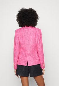 Růžový tvídový blejzr s přiléhavým střihem, strukturovanými rameny, rozventilováním vzadu a zlatými knoflíky na manžetách.