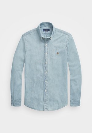 Lyseblå denimskjorte med knepping på kragen, lange ermer og klassisk passform. Har et lite brodert emblem på venstre bryst.