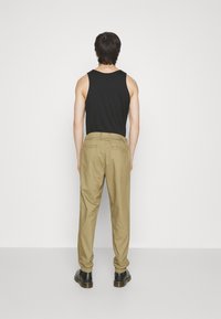 Menns svart ermeløs tanktop kombinert med khaki bukser, som har rett passform og elastiske mansjetter ved anklene. Svarte sko fullfører antrekket.
