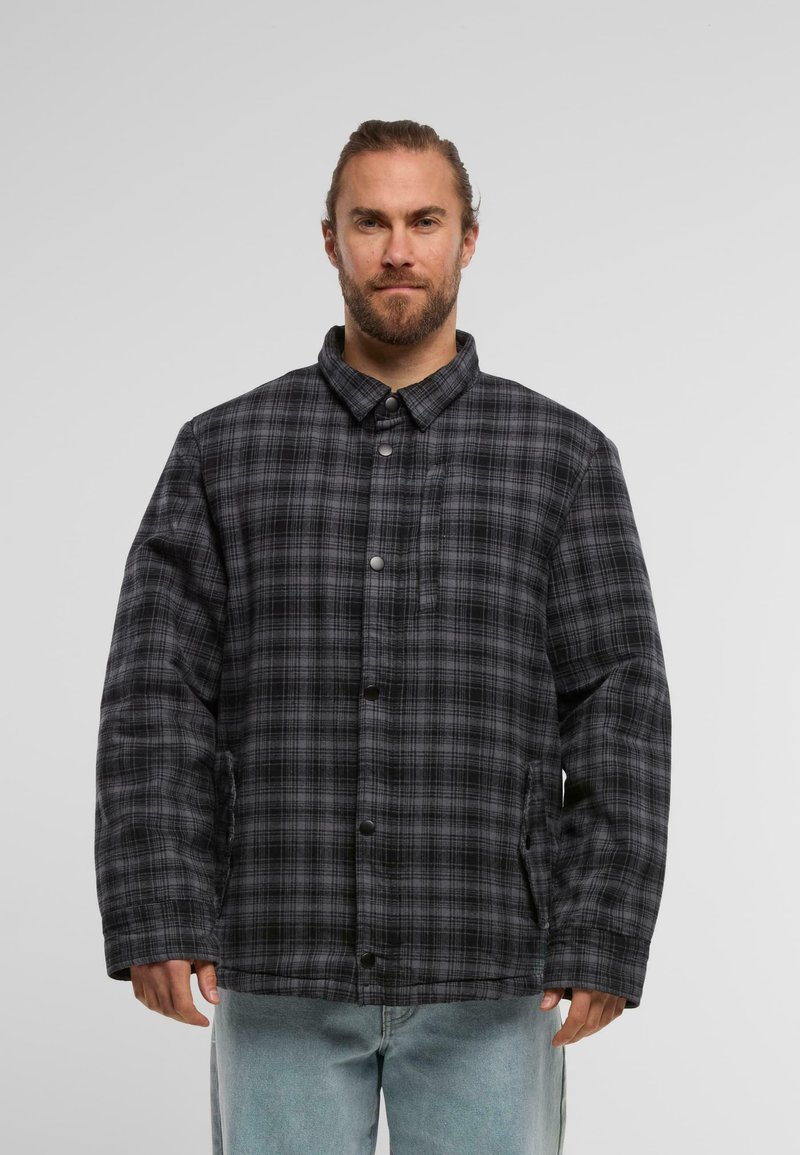 Melnā un pelēkā laukuma raksta jaka ar pogu aizdari, stāvošu apkakli un sānu kabatām. Iezīmē brīvu piegriezumu un quilted tekstūru.