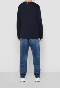 Marinblå långärmad skjorta, blå denimjeans och vita sneakers med svarta och röda accenter. Skjortan har en enkel design utan grafik.