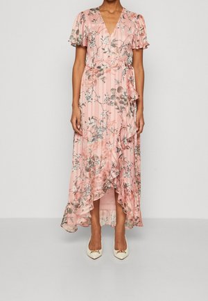 Robe maxi florale en rose doux avec des manches courtes volantées, un décolleté en V, un ourlet volanté et des rayures tonales. Associée à des chaussures blanches à bout pointu.