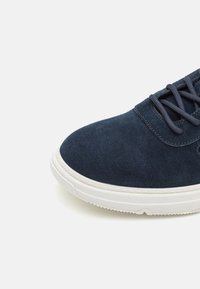 Sneakers din suede bleumarin cu vârf rotund, talpă din cauciuc alb și șireturi bleumarin, având cusături subtile și o textură netedă.