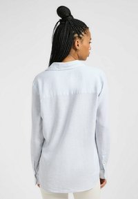 Hellblau gestreifte Button-Up-Bluse mit Kragen und langen Ärmeln, mit abgerundetem Saum und dezenter Textur.
