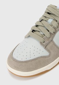 Lys grå læder og taupe ruskind sneaker med perforeret tåboks, flade snørebånd og gummisål. Har kontrastsyede detaljer.