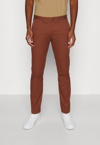 Brown slim-fit trousers made of cotton, featuring a classic button closure, side pockets, and a smooth fabric texture. Paired with white sneakers.