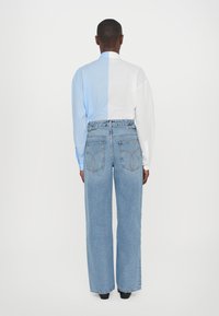 Blue and white color-block shirt with long sleeves, paired with high-waisted, wide-leg blue jeans featuring back pockets and stitching details.
