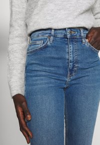 High-waisted blue denim jeans with a classic fit, featuring a five-pocket design and subtle stitching, seen alongside a gray knitted sweater.
