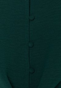 Dark green fabric featuring a row of three buttons along the center, with smooth texture and subtle stitching details.