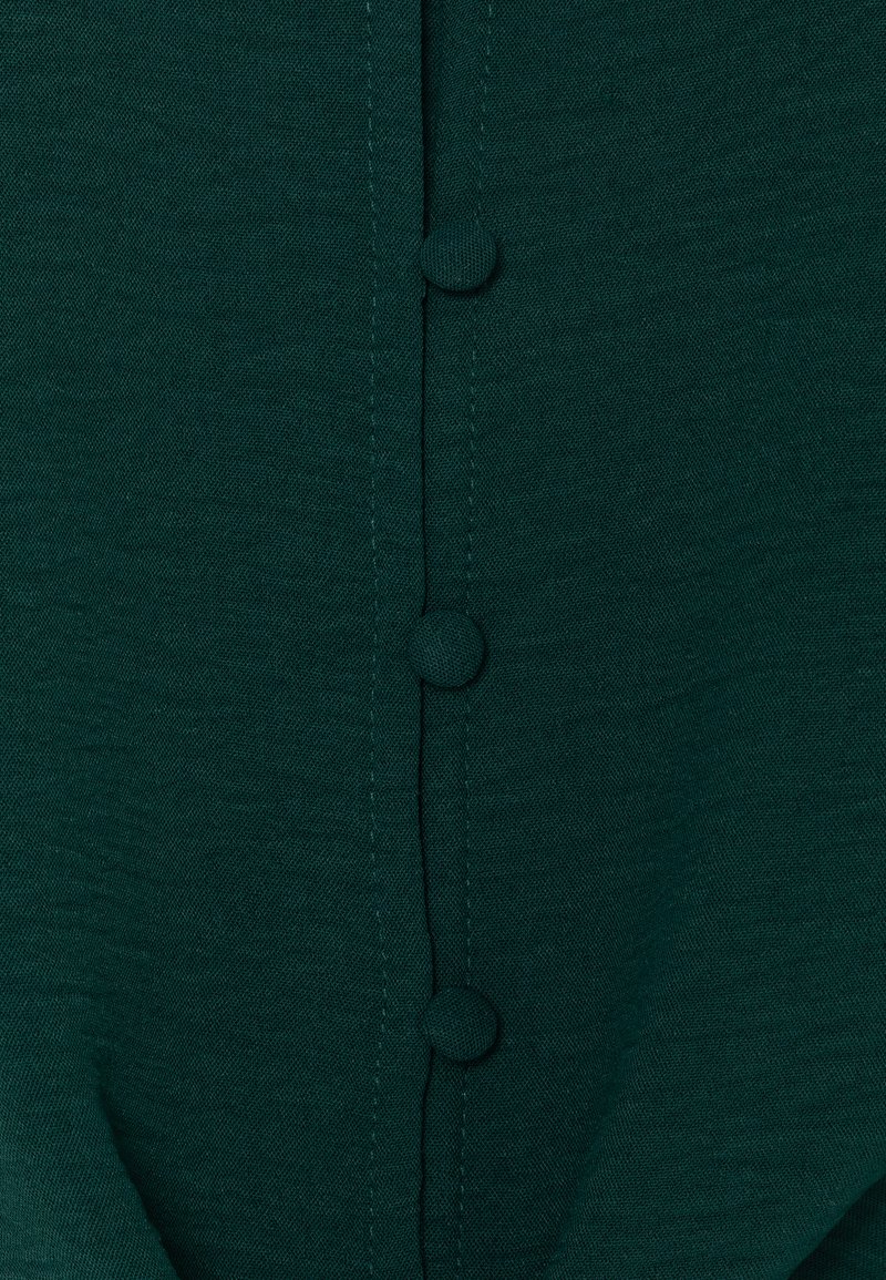 Dunkelgrüner Stoff mit einer Reihe von drei Knöpfen in der Mitte, mit glatter Textur und dezenten Stickdetails.