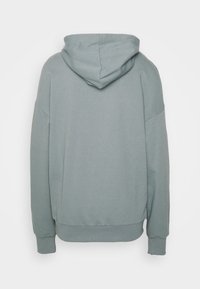 Mjuk, ljusgrå huvtröja sedd bakifrån med långa ärmar, ribbade muddar och en ribbad midja.