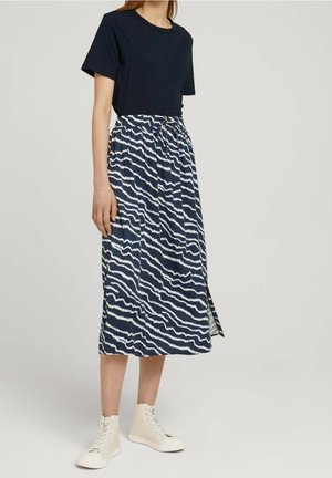 Marineblå T-shirt kombineret med en maxinederdel med blomsterprint, der har hvide bølgede linjer og bundet talje, båret med off-white snøresko.