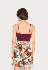 Top cropped burgundy com alças finas combinado com calções creme que apresentam um vibrante padrão floral tropical em tons de laranja e verde.