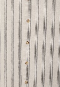 Chemise en tissu rayé crème avec fines rayures noires. Présente des boutons ronds beige sur le devant avec une finition texturée.