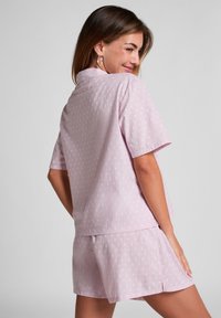 Lichtroze pyjamaset met korte mouwen en een korte broek, met een gestippelde textuur en een relaxte pasvorm. Eenvoudige kraag en zijopeningen.