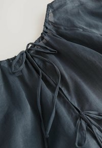 Donkergrijze lichte blouse met een geraffineerde halslijn en striksluitingen, gemaakt van zacht, vloeiende stof.