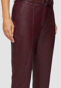 Burgundy läderbyxor med en slät yta, med rak passform och sidofickor. Ett bälte är synligt vid midjan.